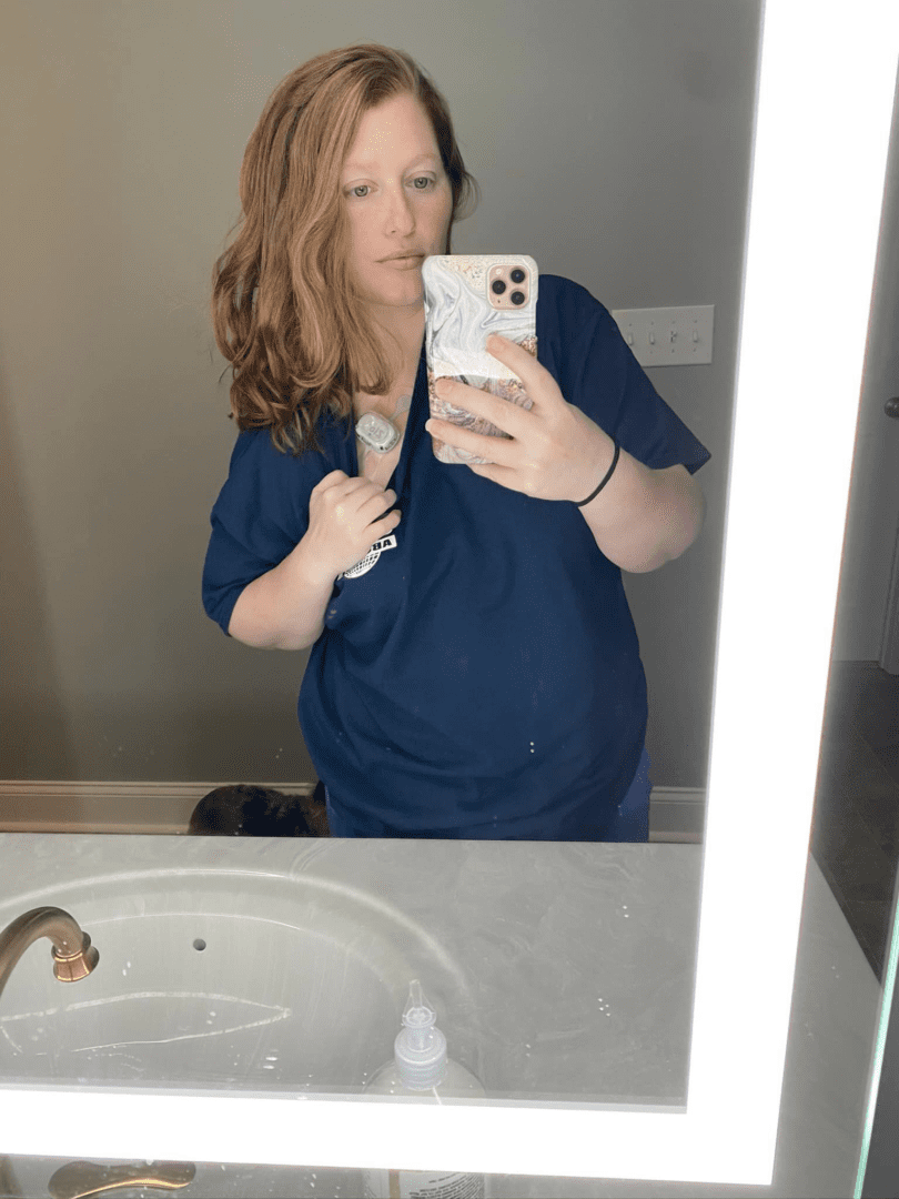 Woman in scrubs taking selfie in bathroom.